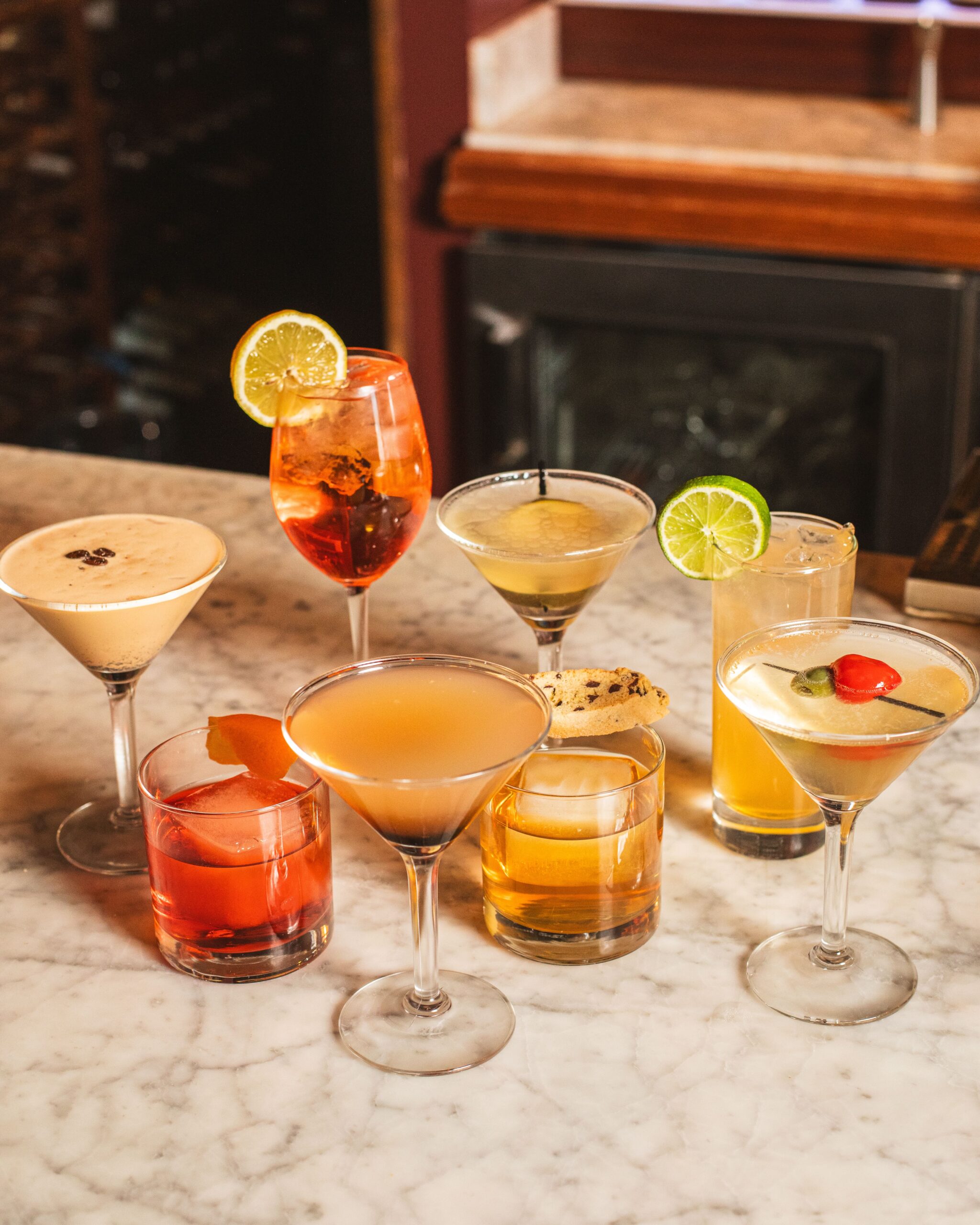 a large group of cocktails on a marble bar in various glasses
