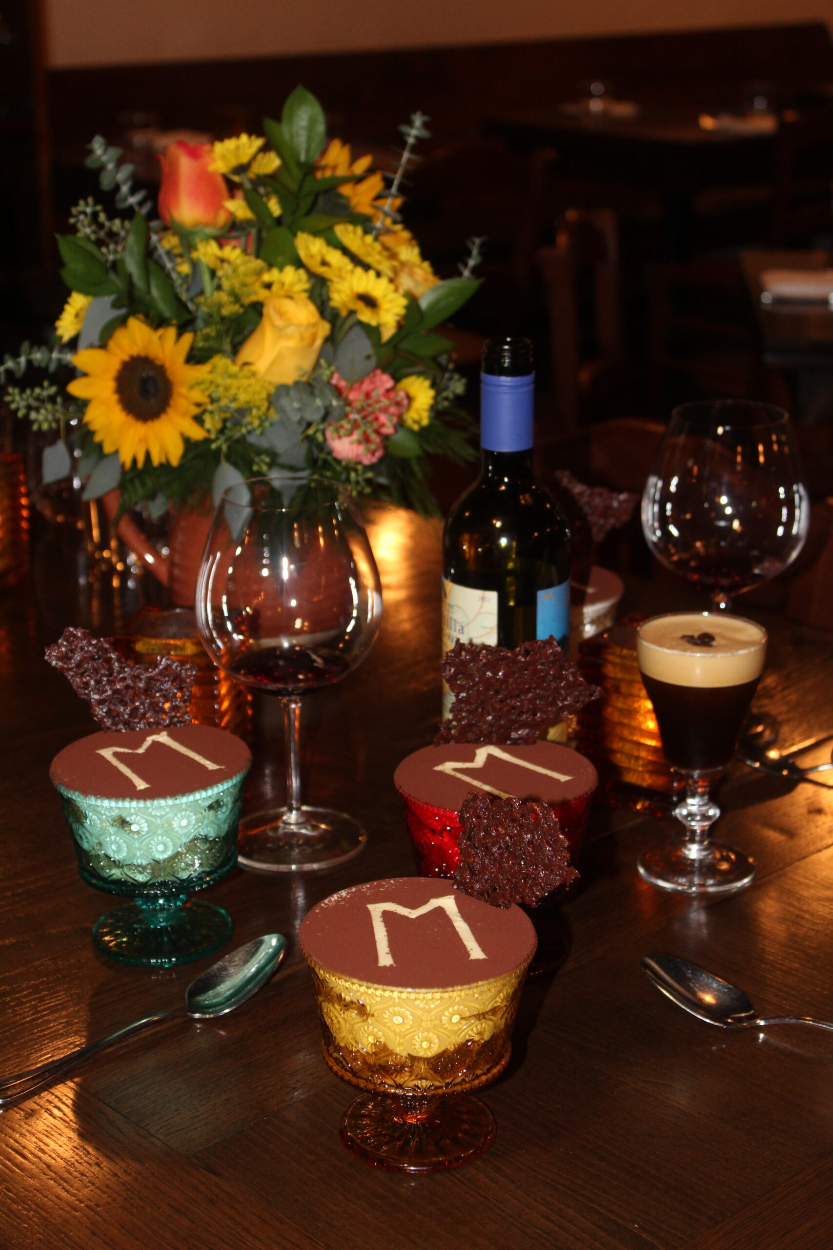 a table with flowers, tiramisus, a bottle of wine, espresso martinis