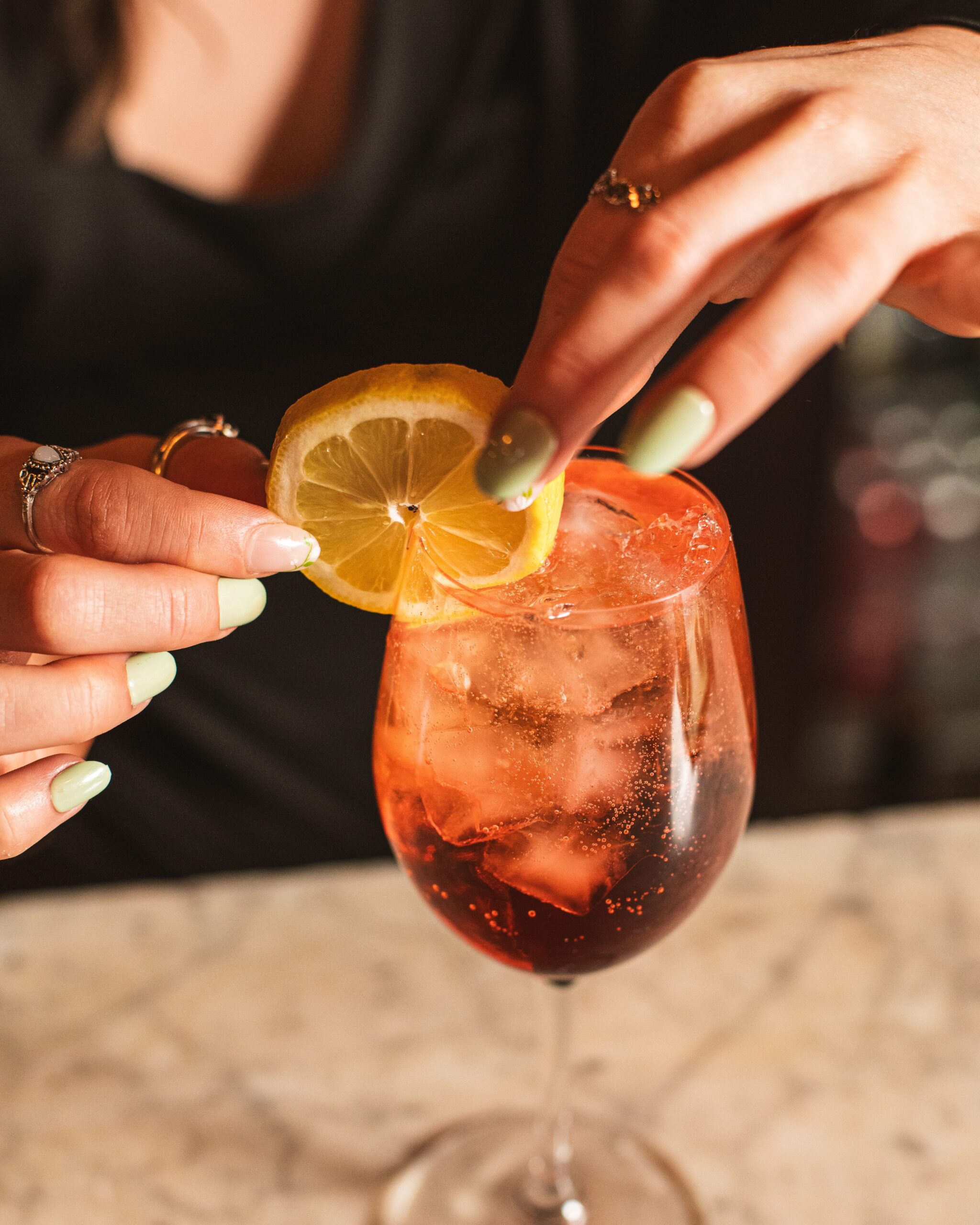 a bartender adding a lemon garnish to an aperol spritz