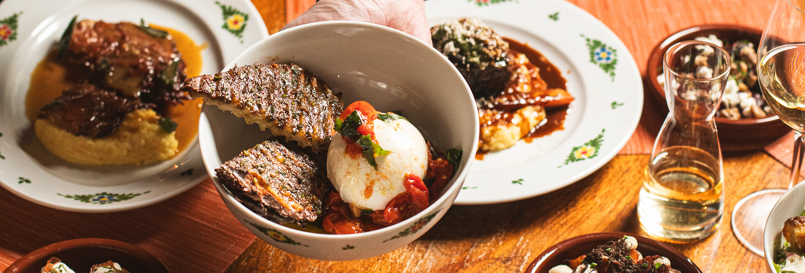 a hand holding a bowl with burrata and crostata