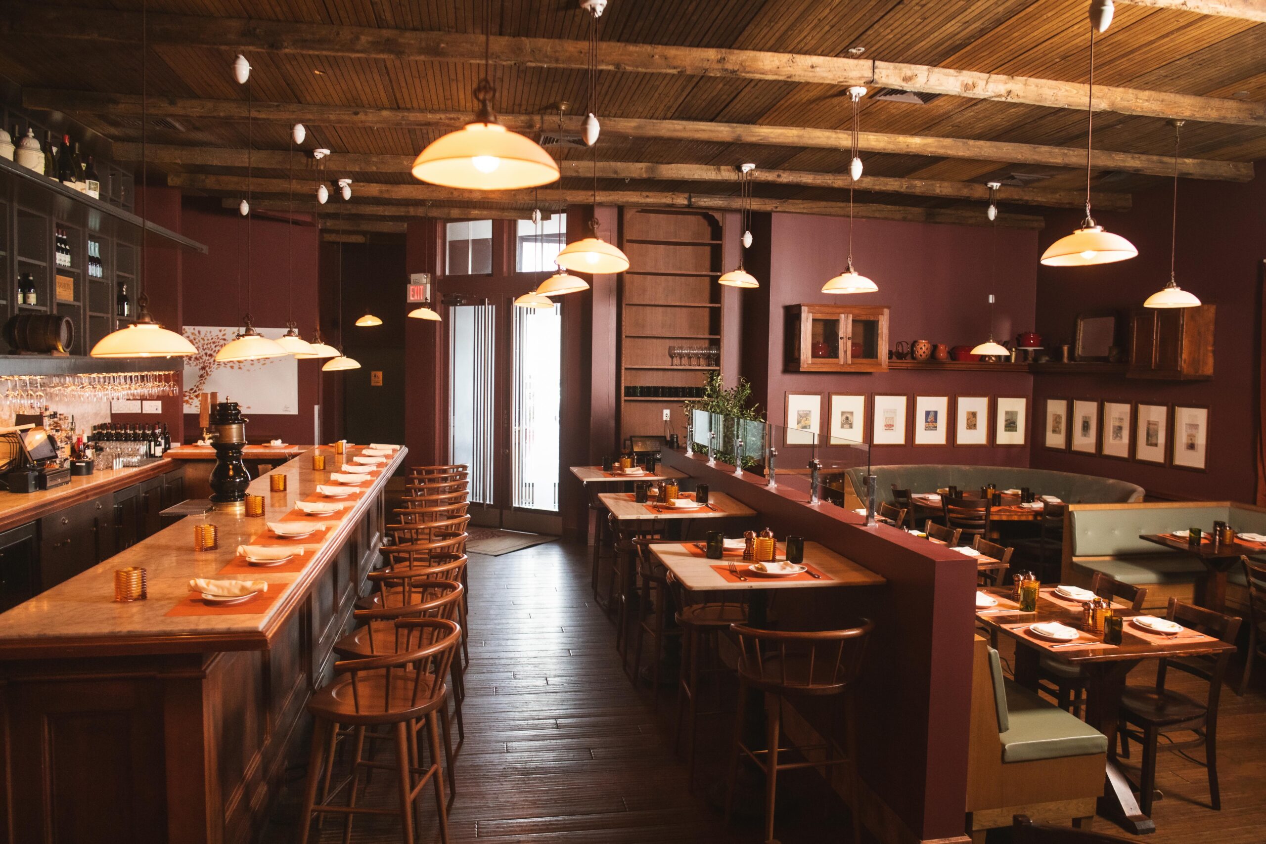 the interior of osteria morini bernardsville - a marble topped bar to the left with wooden stools. across from that is 3 high top tables. to the right, light green leather banquets with wooden tables. the ceilings are wooden slats and the walls are painted dark maroon.