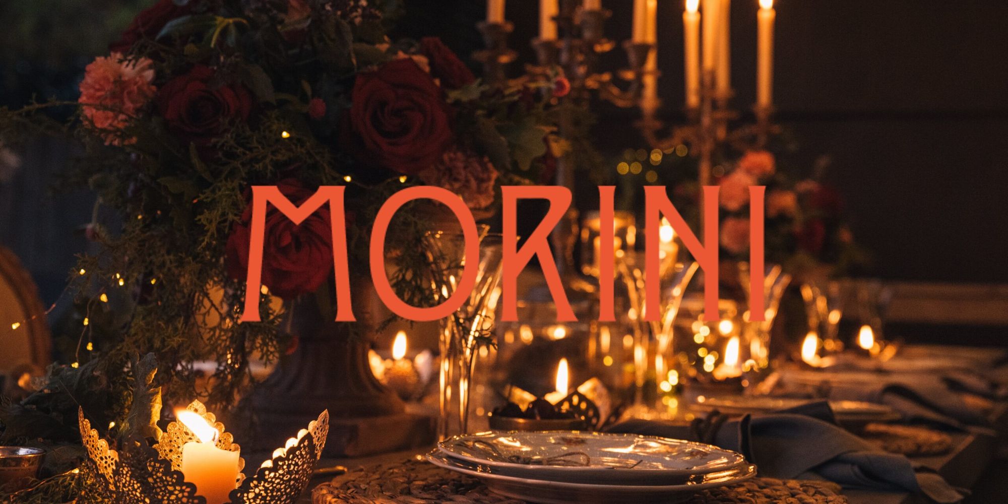 A candlelit table set with red roses and tall candles, the word Morini across it.