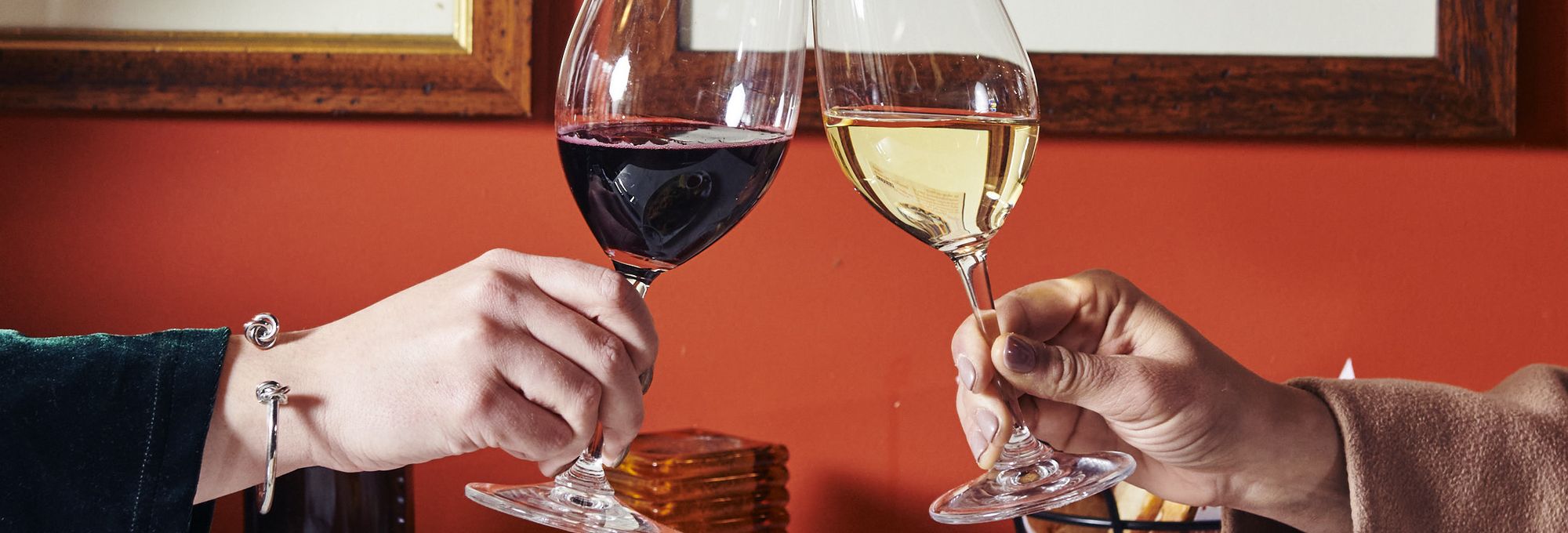 two people cheers-ing a glass of red wine and a glass of white wine