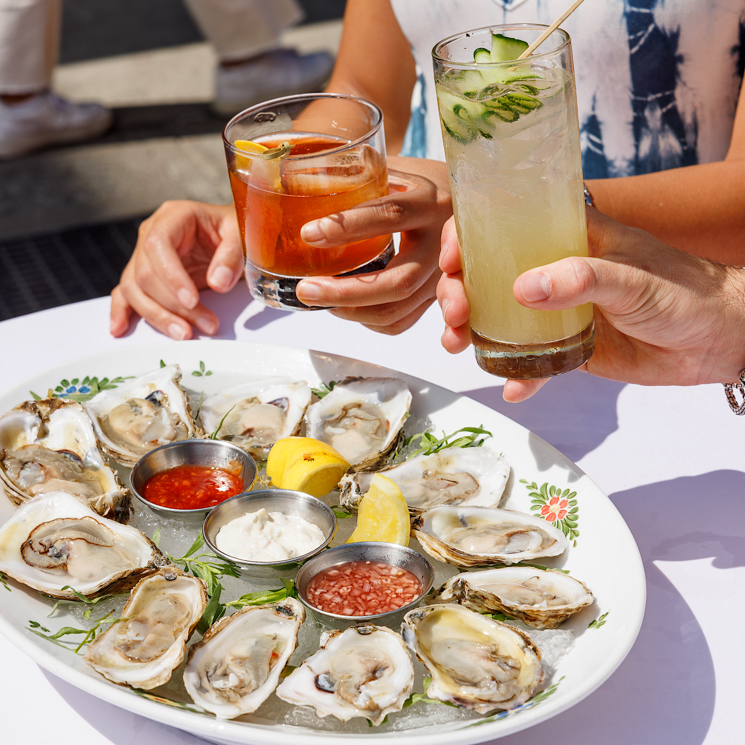 two people cheers cocktails over a plate of oysters