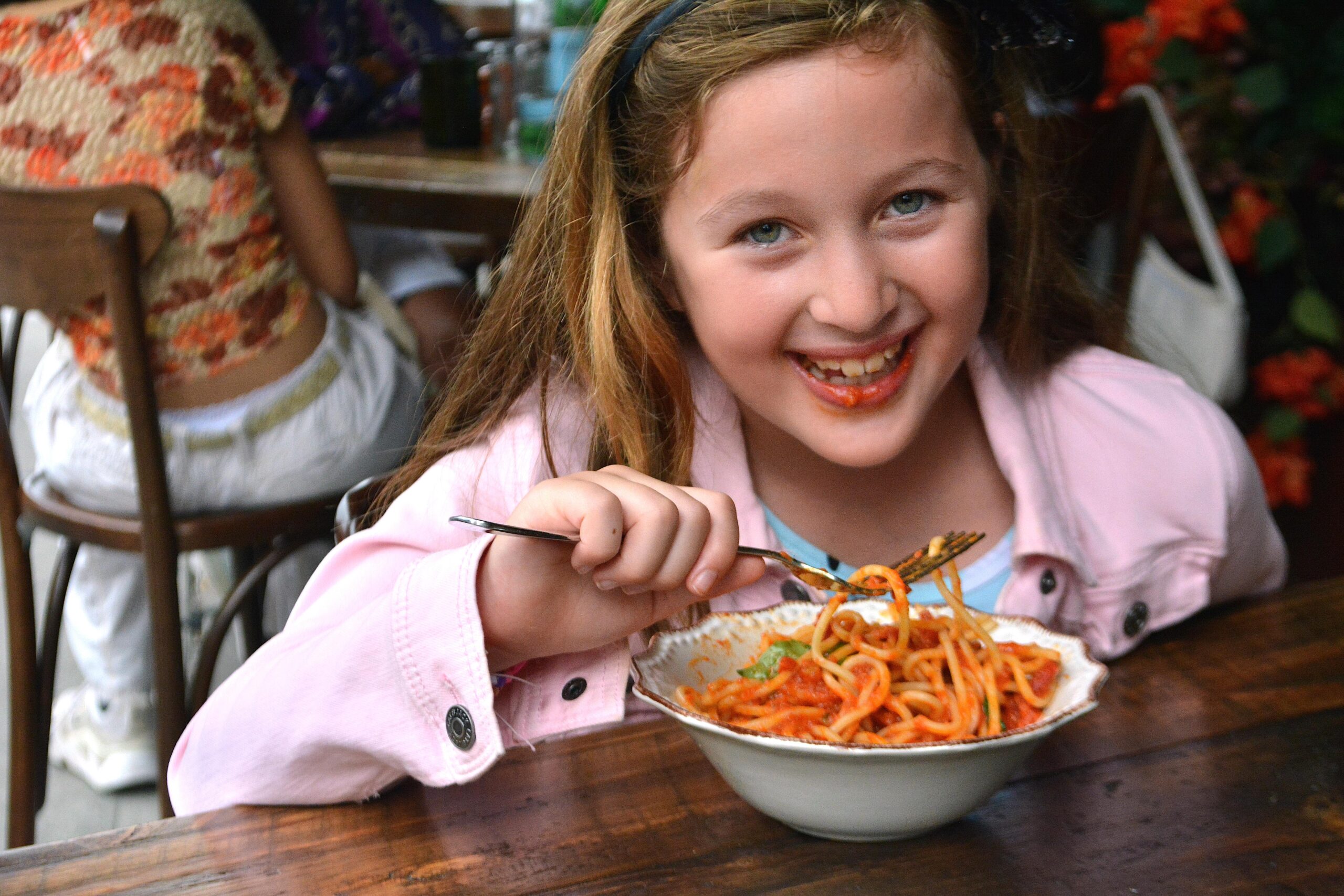 a young girl eating a bowl of pasta
