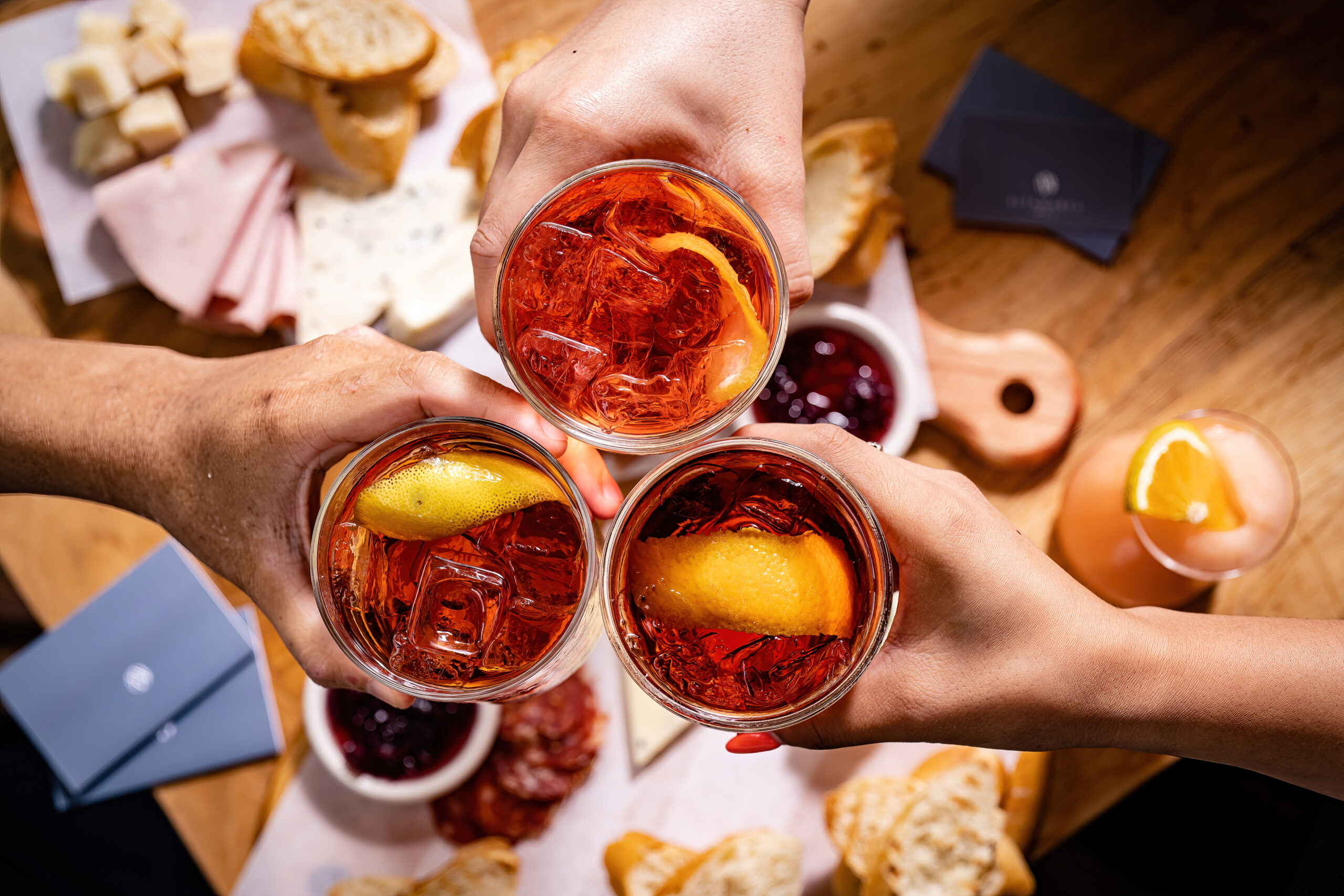 three people cheersing negronis over a table full of battilardo - meat and cheese boards